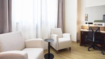 Habitación de hotel moderna con sofá, sillón, una mesita redonda y un escritorio con silla.
