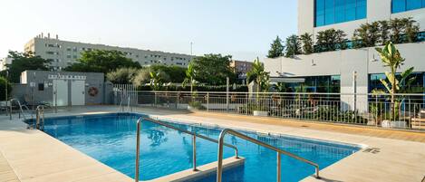 A swimming pool with a lifeguard stand, a fence, and a building with large windows in the background.