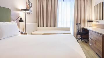Een hotelkamer met een groot bed, een bureau, een stoel, een lamp en een raam met gordijnen.