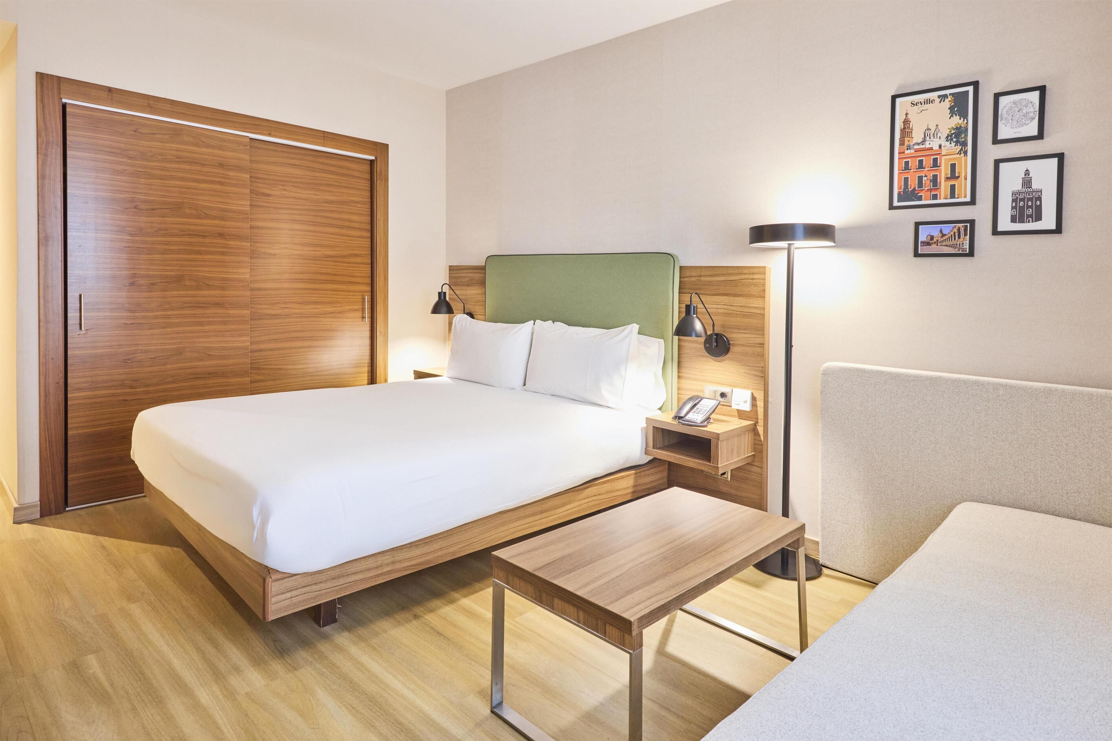 Quarto de hotel com cama, mesa de cabeceira, luminária e obra de arte na parede.