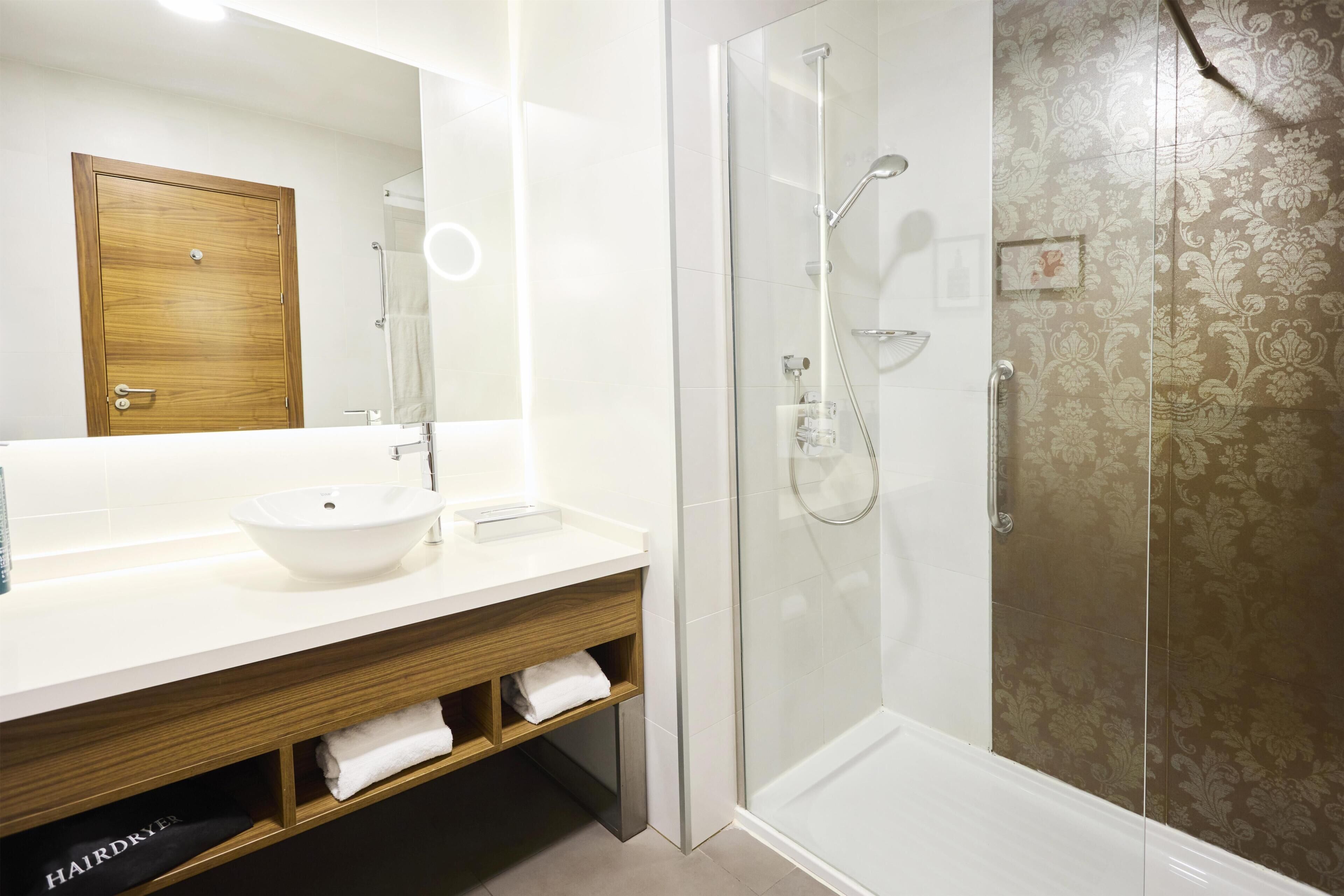Une salle de bain avec un lavabo blanc, un miroir et une douche à parois de verre.