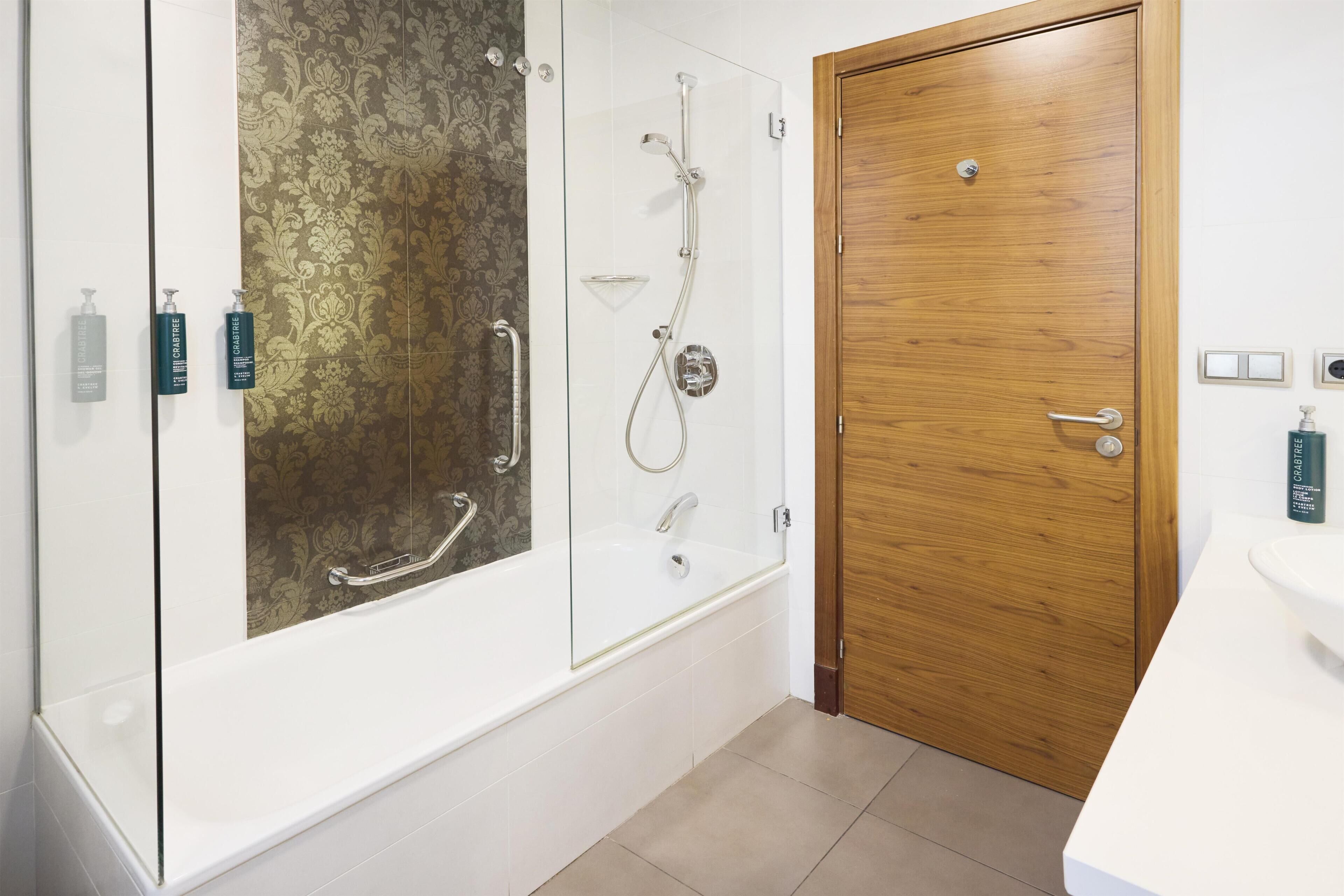 A modern bathroom with a glass-enclosed shower, a wooden door, and a white sink.