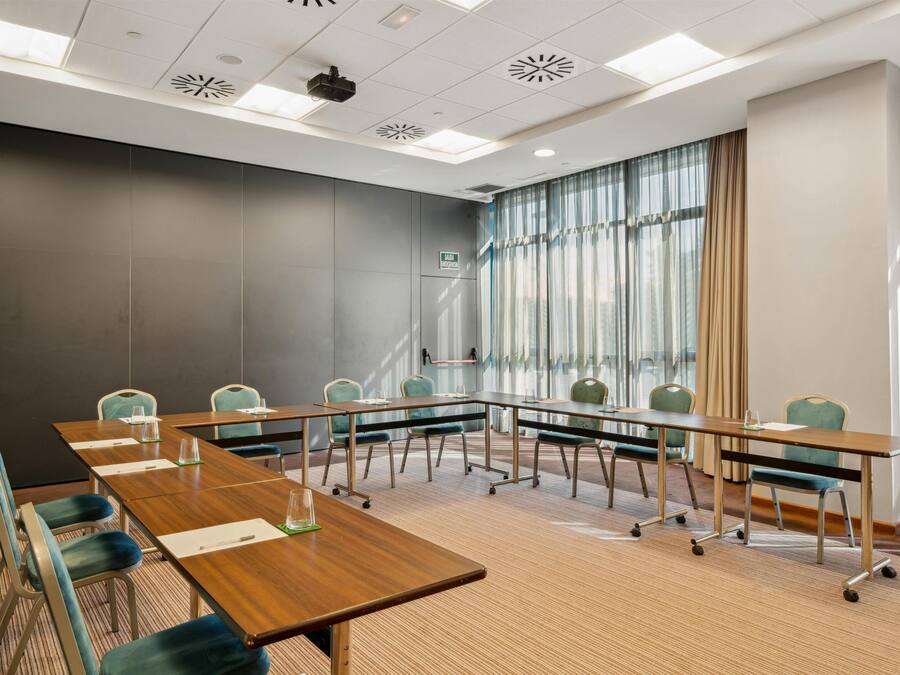 Une salle de conférence avec une longue table, des chaises, un projecteur et une fenêtre avec des rideaux.