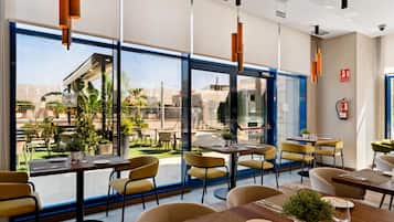 A modern restaurant with large windows, yellow chairs, and wooden tables.