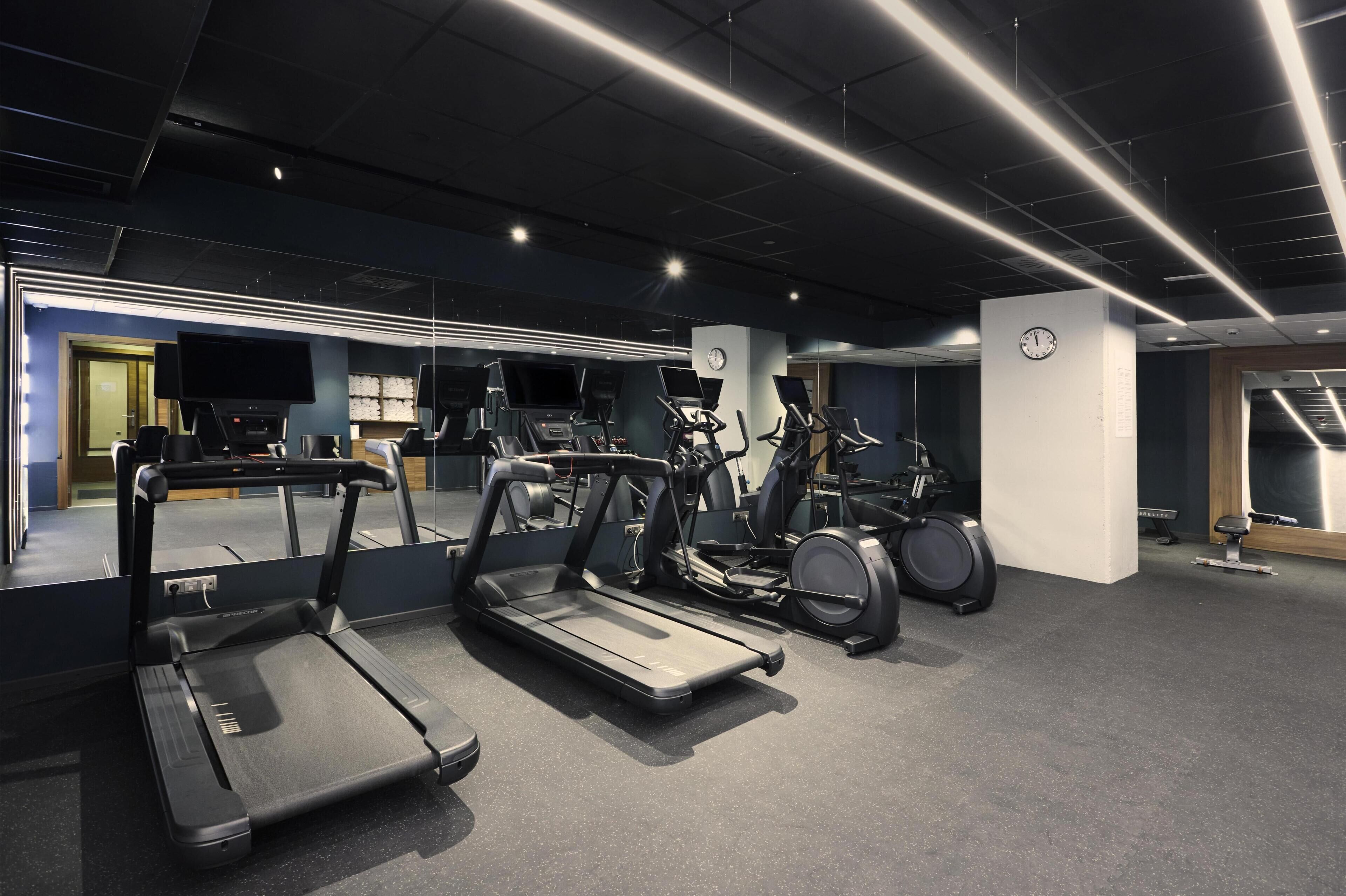 Un gimnasio con cintas de correr, elípticas y un reloj en la pared.