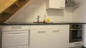Eine Küche mit weißen Schränken, einem Edelstahlbackofen und einer Holztreppe.