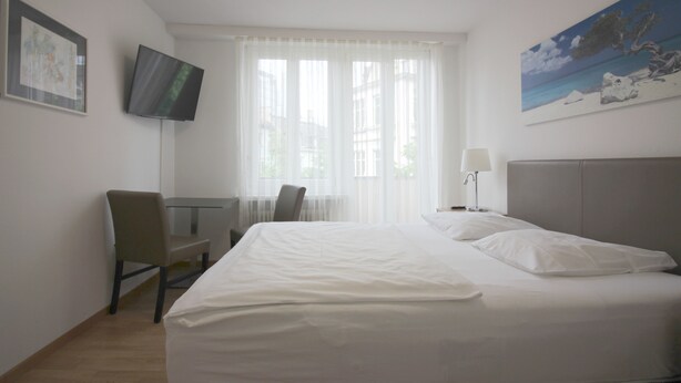 Ein Hotelzimmer mit einem Bett, einem Schreibtisch, einem Stuhl, einem an der Wand montierten Fernseher und einem Bild an der Wand.
