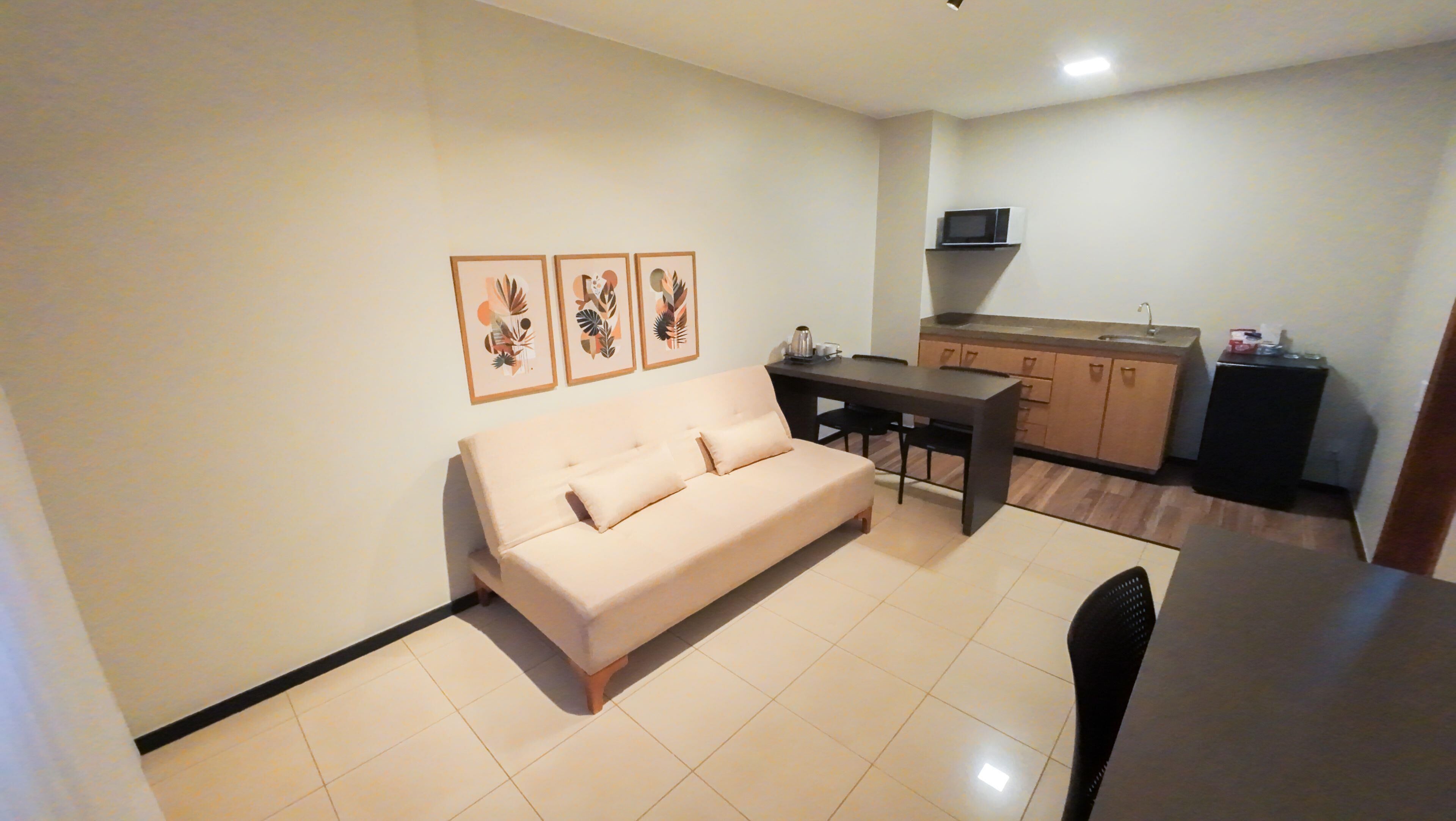 A living room with a sofa, a dining table, and a kitchen area with cabinets and a microwave.