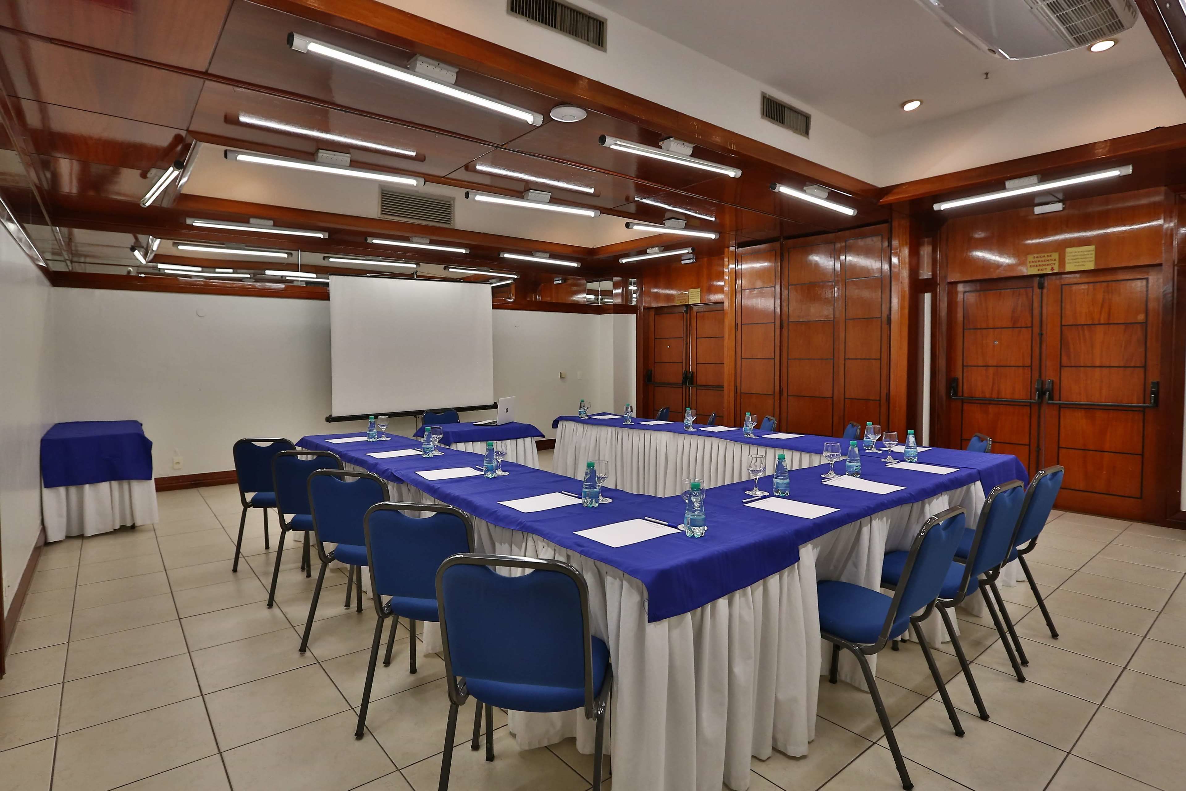 Uma sala de conferências com uma mesa comprida, cadeiras azuis e toalhas de mesa brancas.