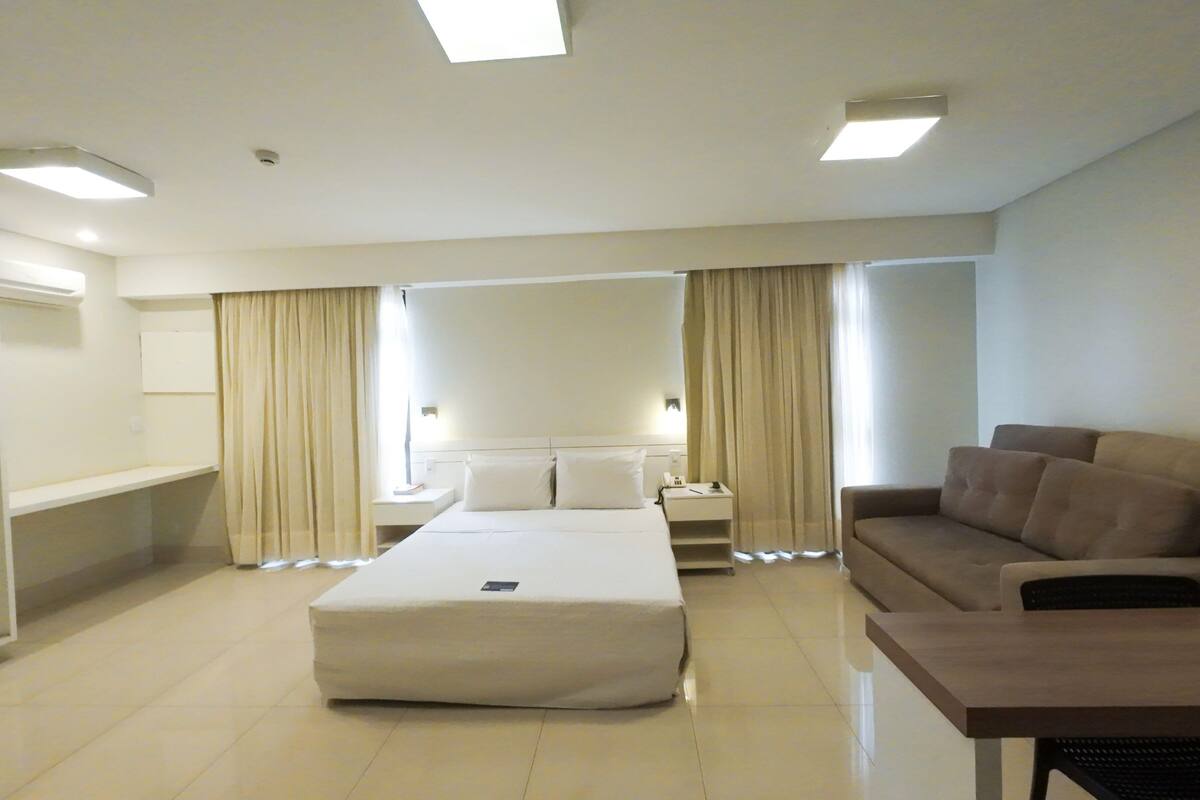 A hotel room with a bed, a sofa, a bedside table, and a wardrobe.