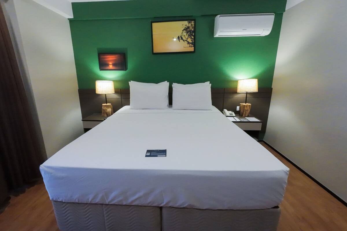 A hotel room with a large bed, two bedside lamps, a nightstand with a phone, and a wall-mounted air conditioner.