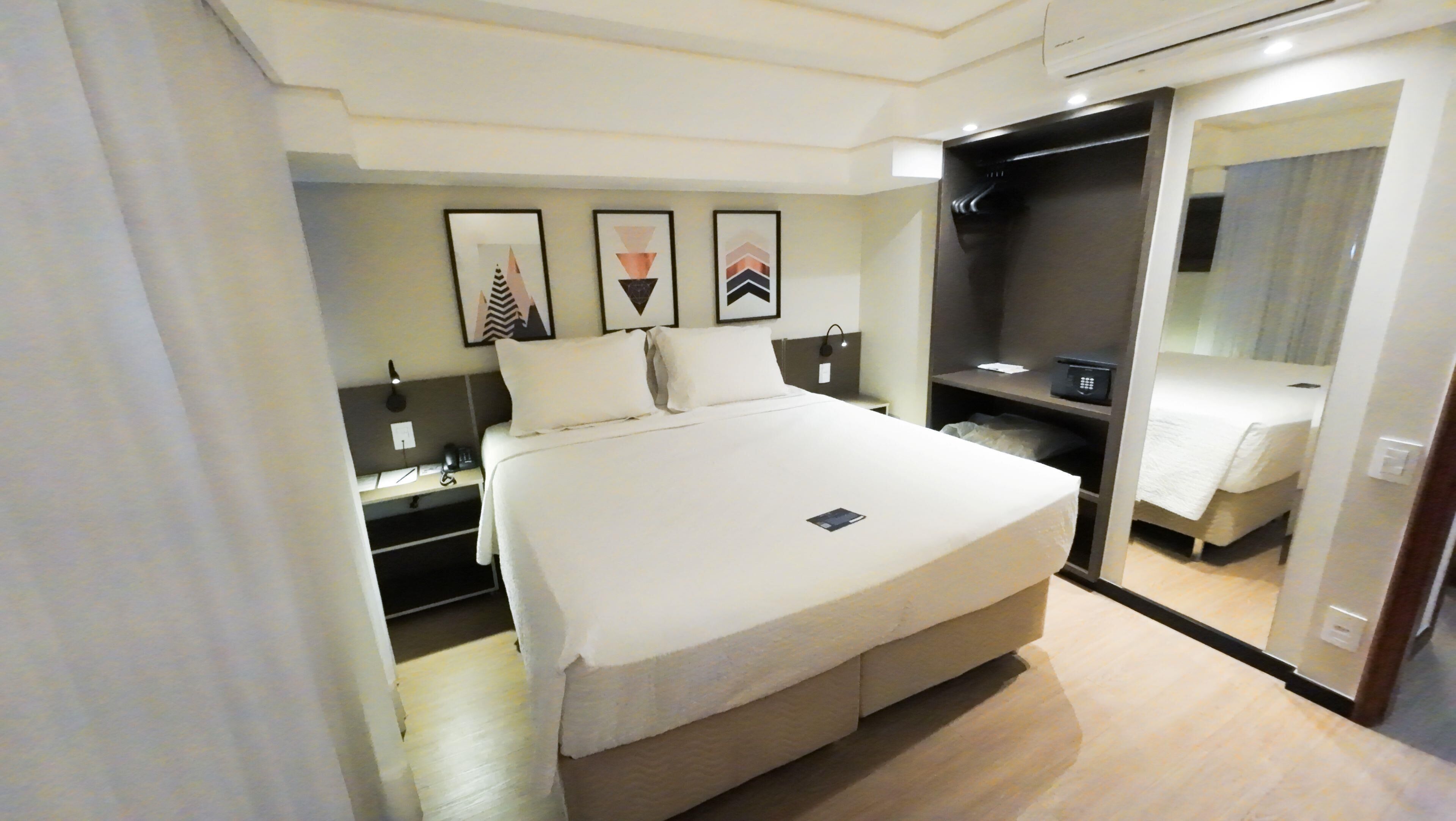 Quarto de hotel moderno com uma cama grande, um closet espaçoso e um espelho.
