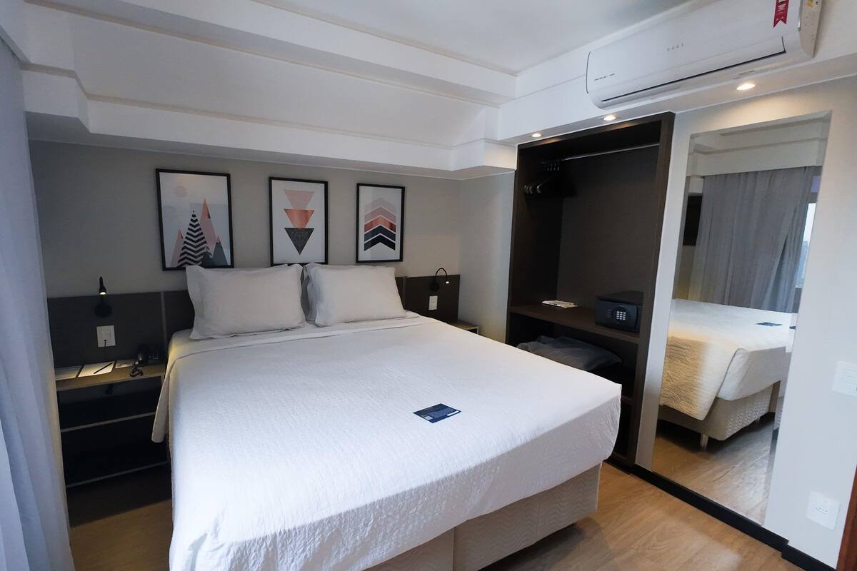 A hotel room with a large bed, a bedside table, a nightstand, a wardrobe, and a mirror.