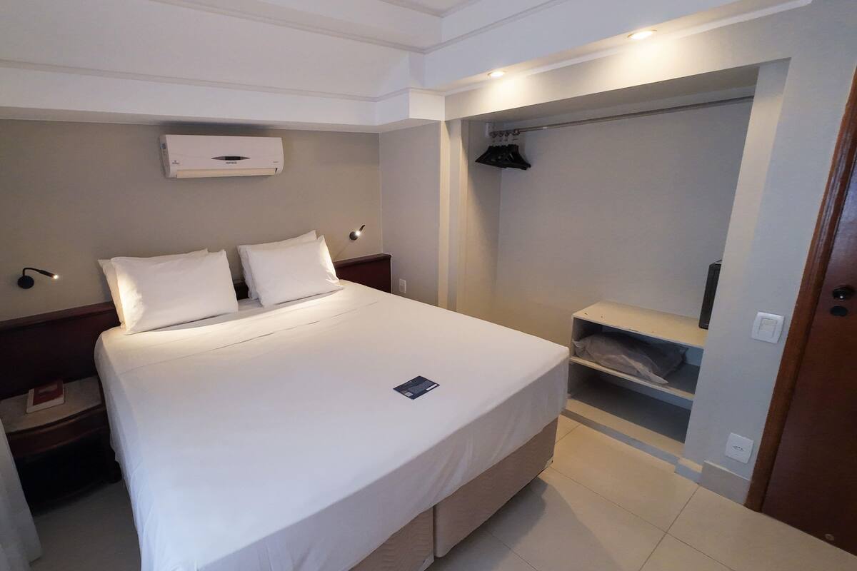 A hotel room with a bed, a nightstand, a wardrobe, and a built-in heater.