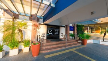 Entrada de hotel con diseño moderno, destacando un frente de vidrio, techo azul y un letrero con la dirección.