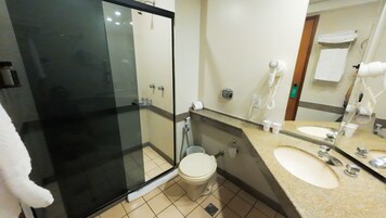 A bathroom with a glass shower enclosure, a toilet, a sink, and a mirror.