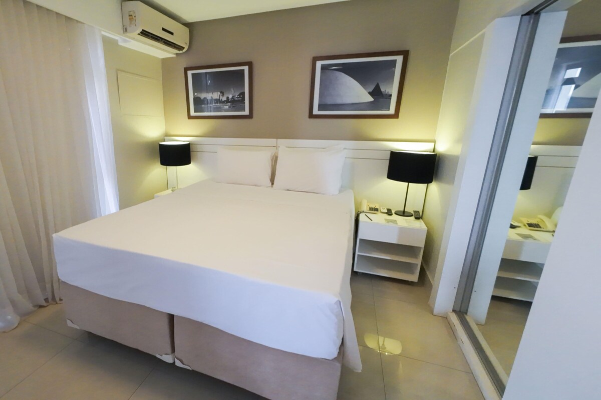 A hotel room with a large bed, two bedside lamps, a nightstand, and a mirror.