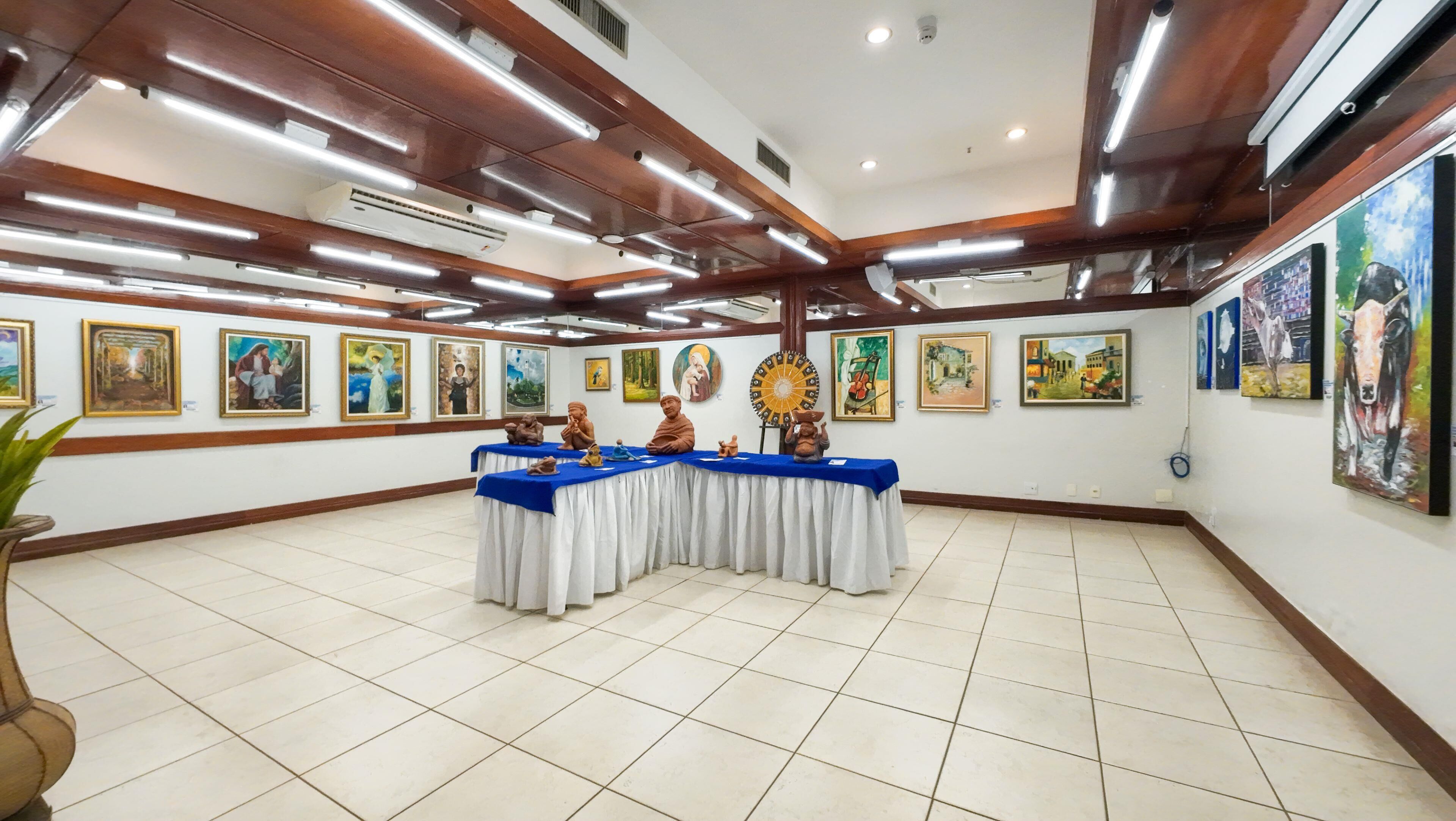 A spacious room with a long table covered with a blue cloth, surrounded by various artworks on the walls.