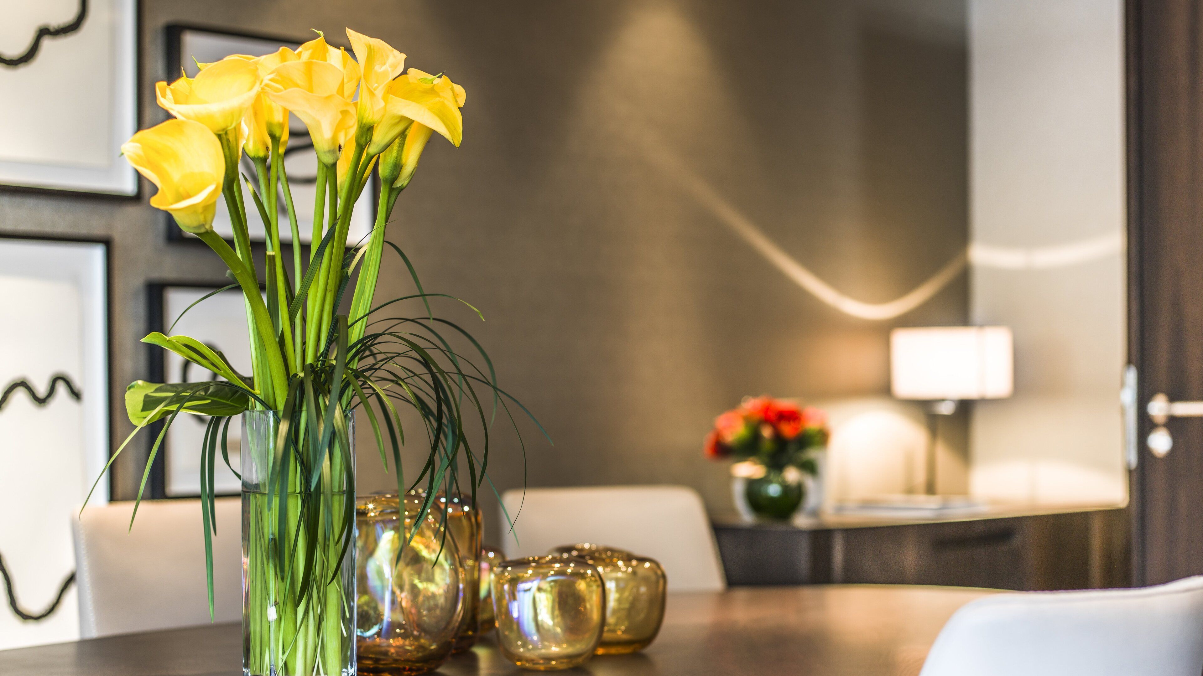 Una mesa de comedor con un jarrón de flores amarillas, un florero de vidrio y un cuenco decorativo.