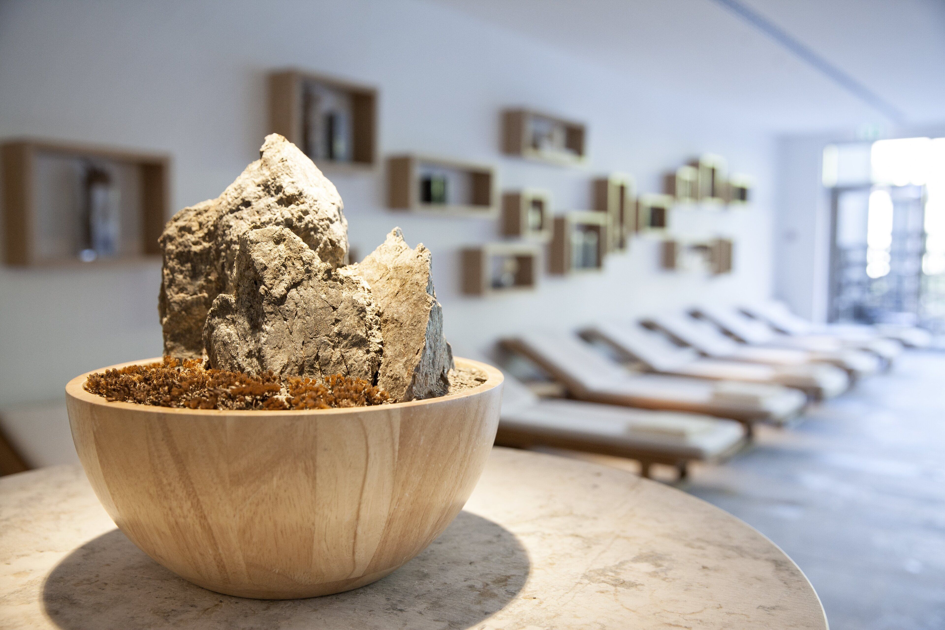 Un cuenco de madera con una escultura de roca sobre una mesa de mármol en una habitación con diseño moderno, que presenta una fila de sillones y obras de arte en la pared.