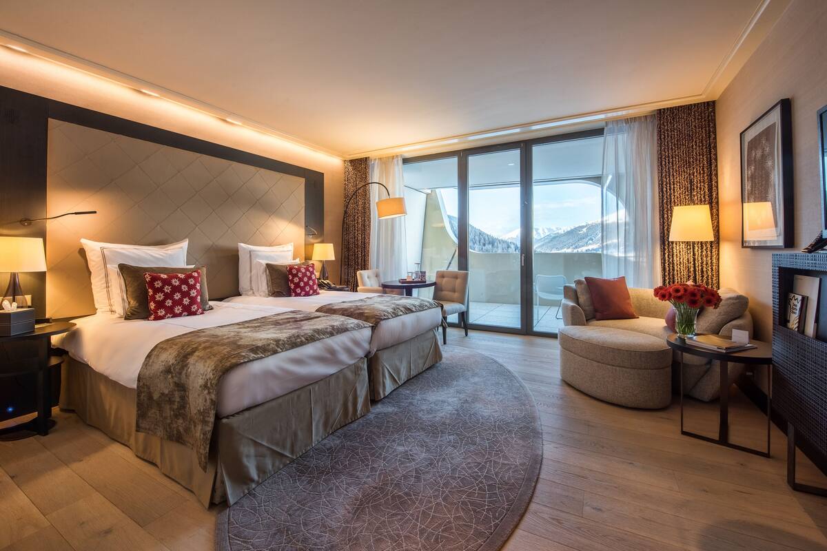 A hotel room with a large bed, a sofa, a desk, and a view of the mountains.