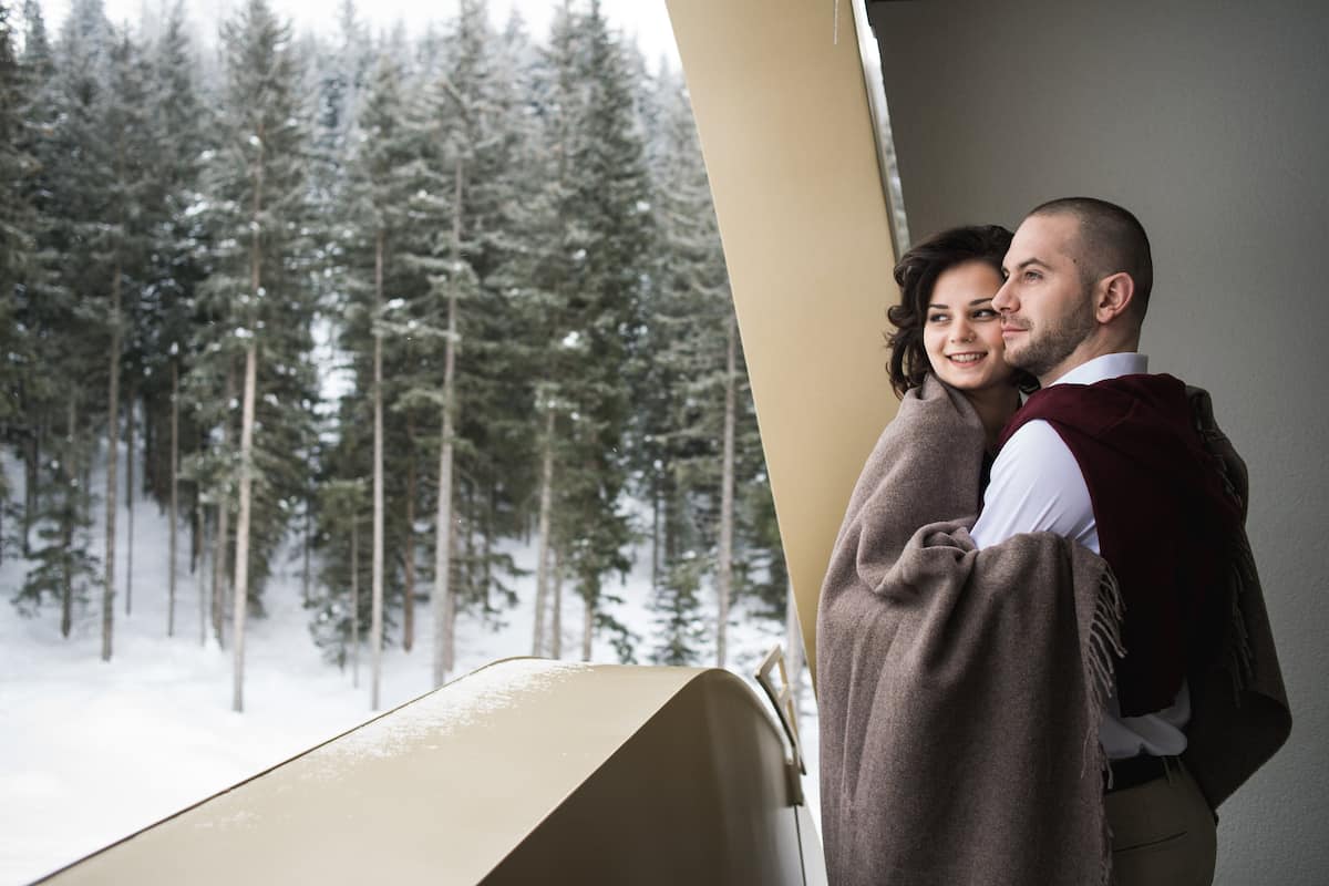 A couple embracing by a window overlooking a snowy forest.
