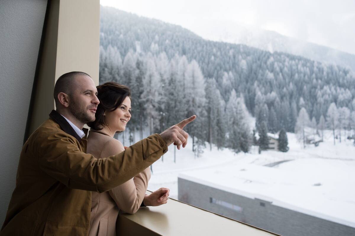 A couple sitting by a window overlooking a snowy forested landscape.
