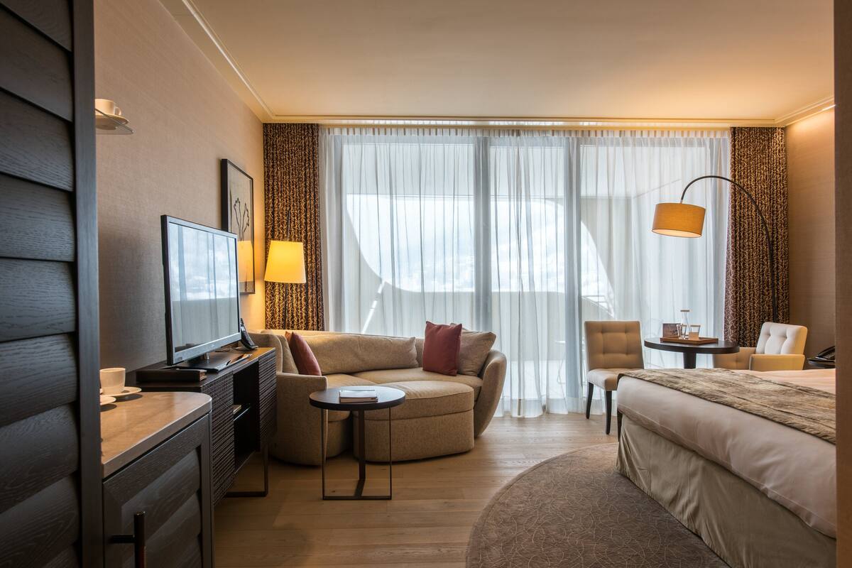 A hotel room with a sofa, a small round table, a bed, a TV, and a lamp.