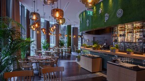 A restaurant with wooden tables and chairs, hanging pendant lights, and a green wall with a bar area. - AlpenGold Davos (Davos)