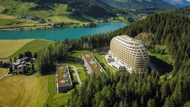 A hotel with a modern design, surrounded by lush green fields and a lake. - AlpenGold Davos (Davos)