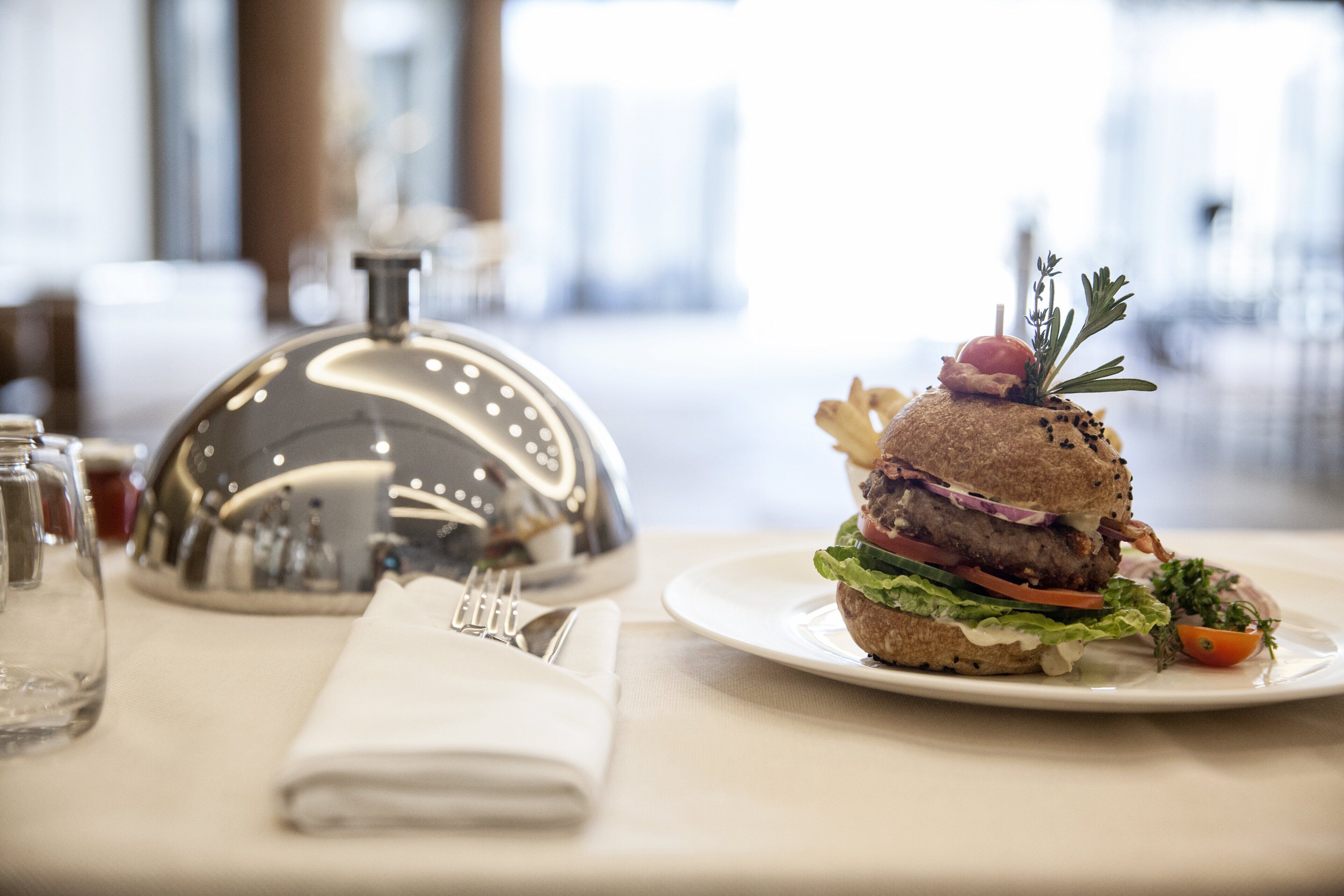 A neatly arranged dining table with a burger, salad, and a silver service bell.