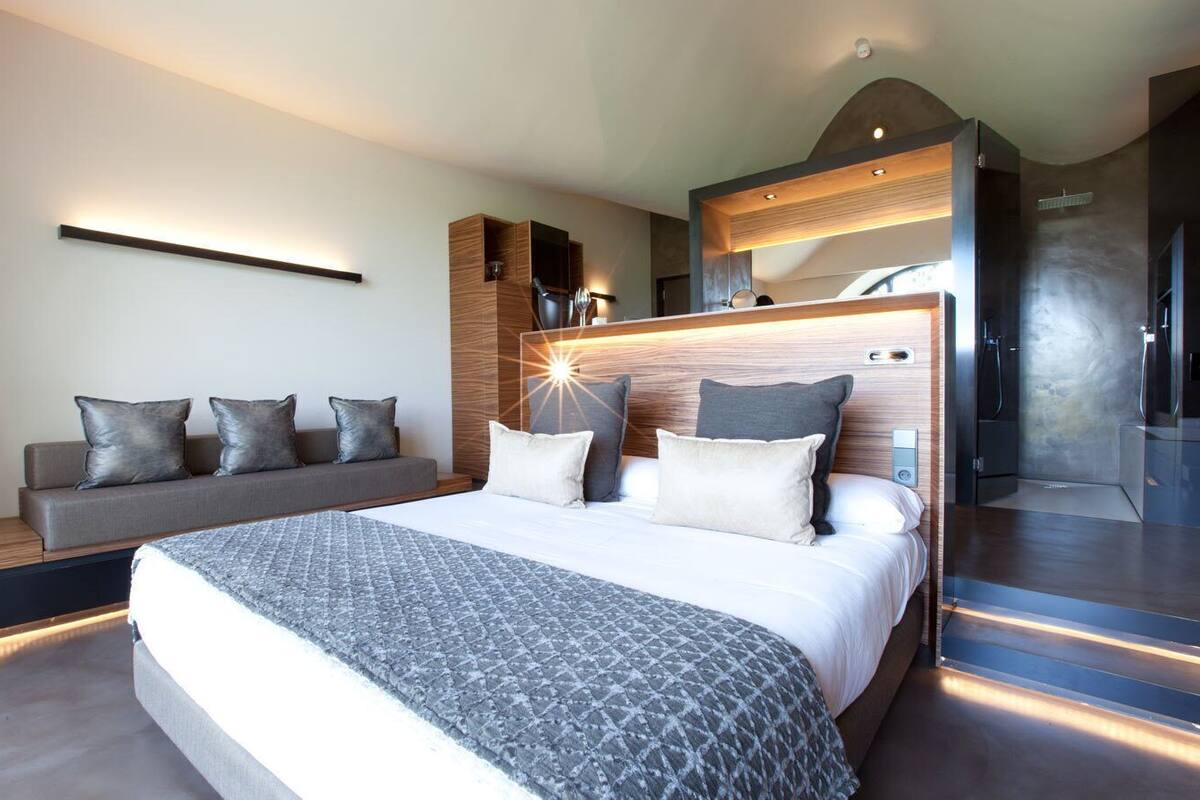 Une chambre d’hôtel moderne dotée d’un grand lit, d’un canapé, d’une douche intégrée et d’un luminaire fixé au mur.