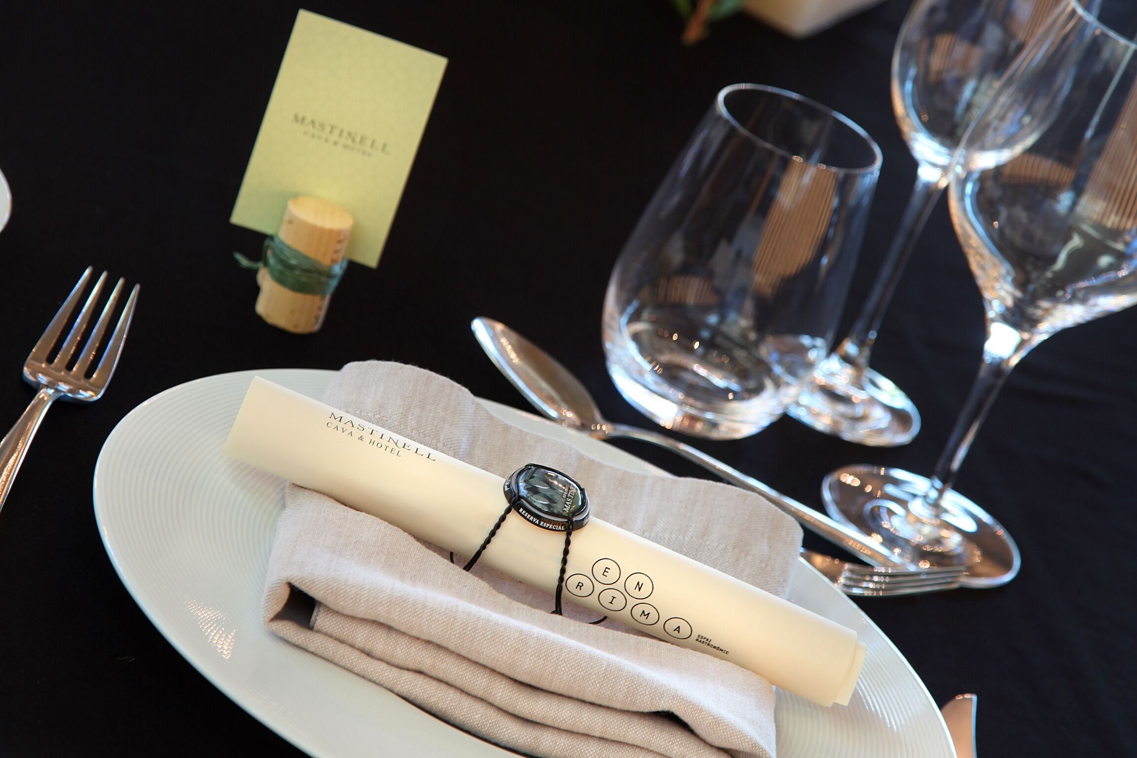 A table set with a folded napkin, a fork, a spoon, and two wine glasses.