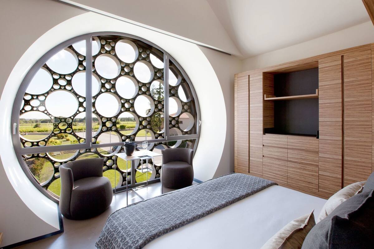 Une chambre dotée d’une fenêtre circulaire, d’un lit, d’un coin salon et de meubles en bois.