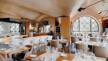 En modern restaurang med en bardel, bord uppdukat med glas och tallrikar, och ett stort, välvt fönster som släpper in naturligt ljus.