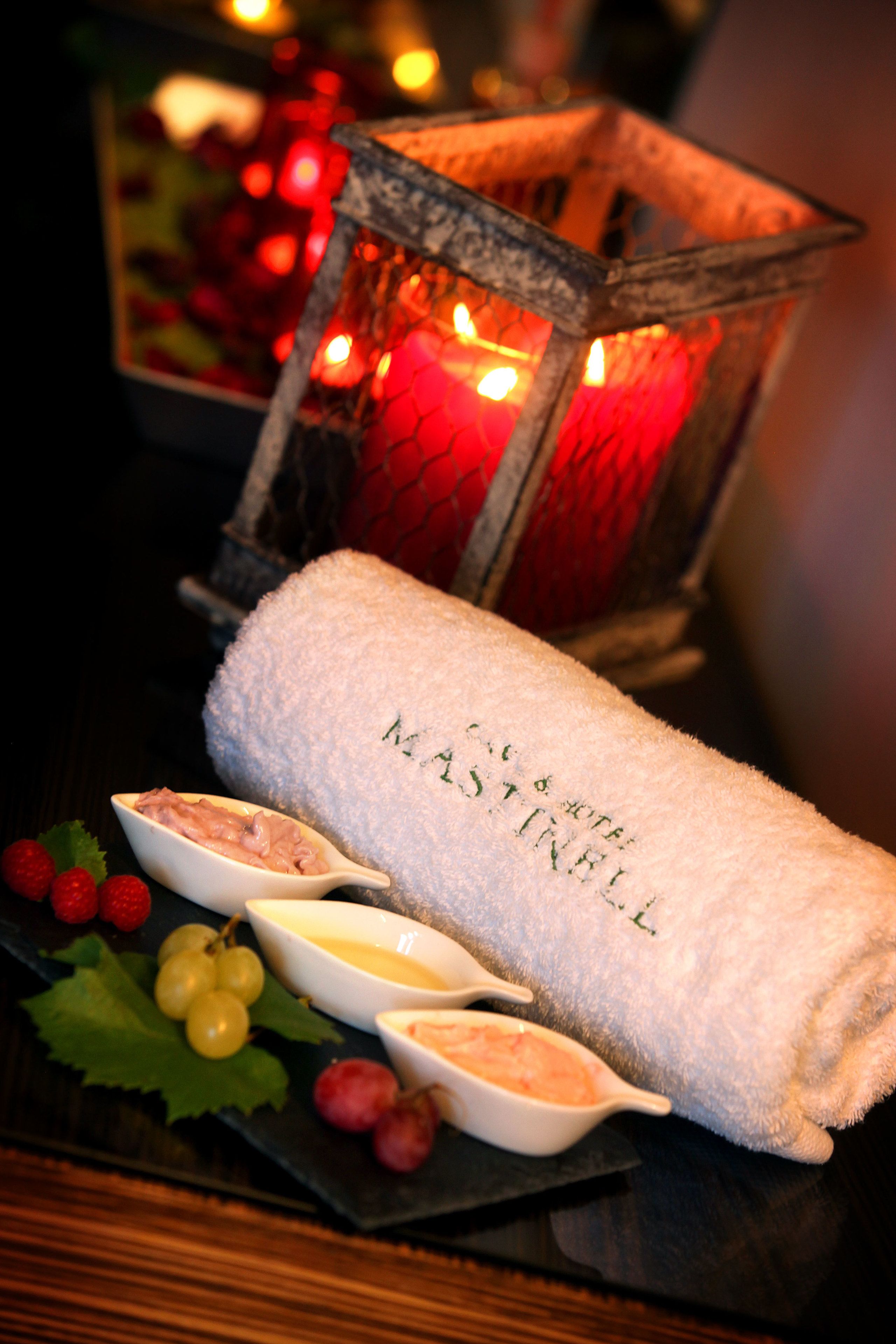 A towel with "Mastrelli" embroidered on it, a small dish with a creamy substance, and a bowl of grapes on a dark surface.