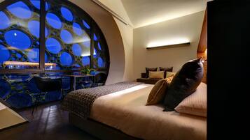 A bedroom with a large bed, a view through a circular window, and a desk with a chair.