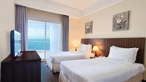 Une chambre d’hôtel avec deux lits, un bureau, une télévision et une grande fenêtre donnant sur la mer.