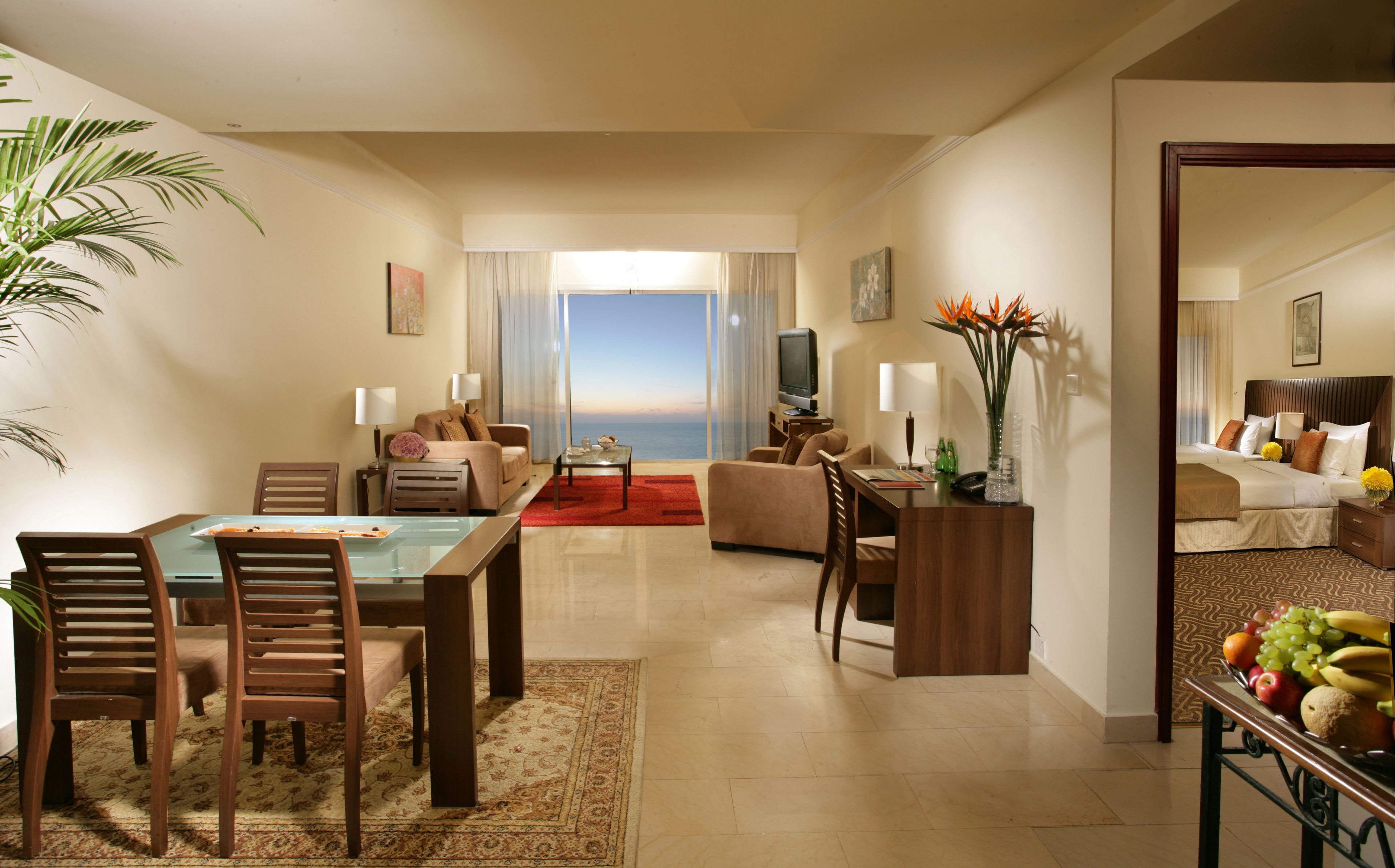Ein Hotelzimmer mit Essbereich, einem Wohnzimmer mit Blick sowie einem Fernseher und einer Obstschale.