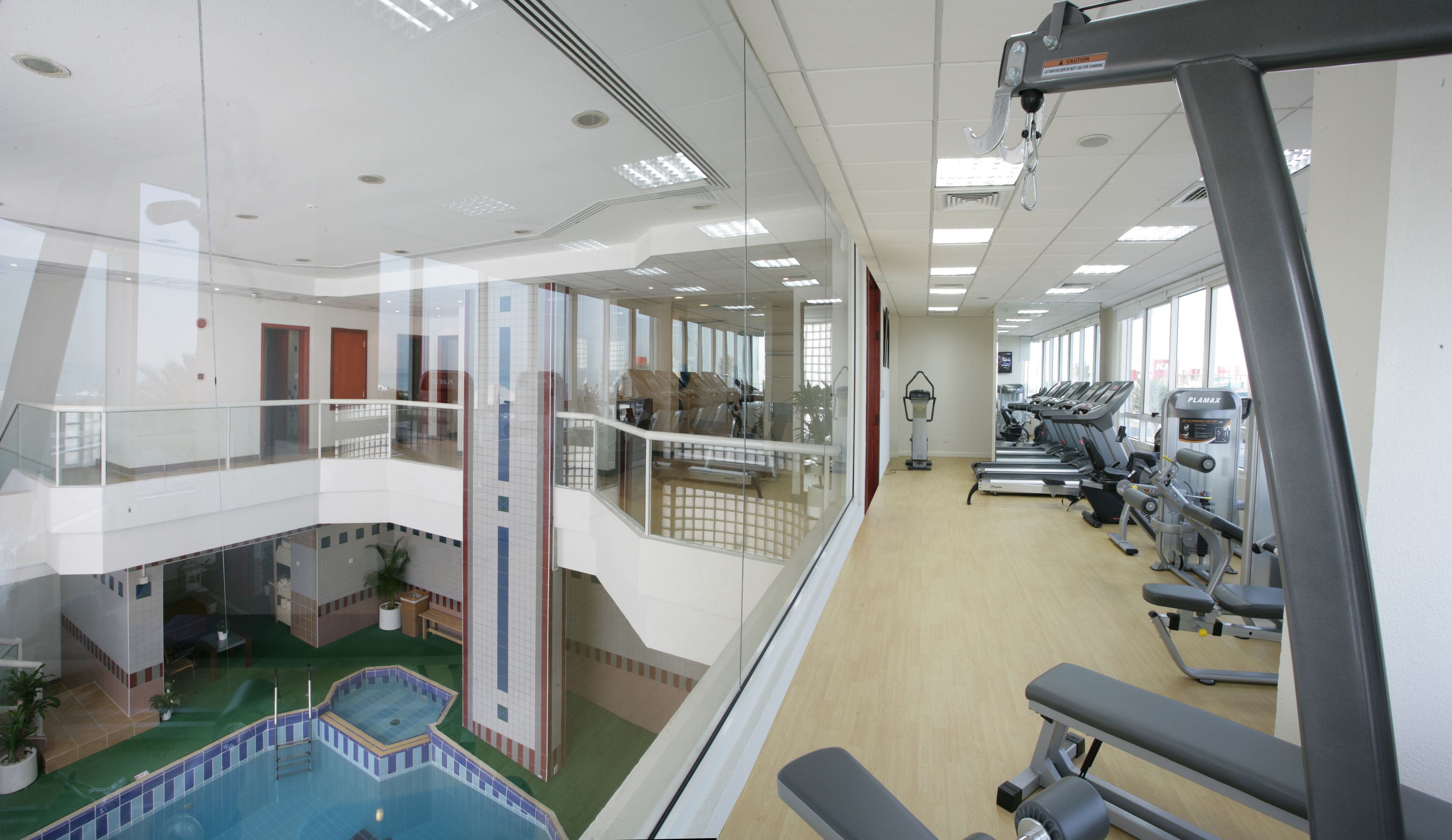 A multi-level indoor facility with a swimming pool, exercise equipment, and a glass-enclosed balcony.