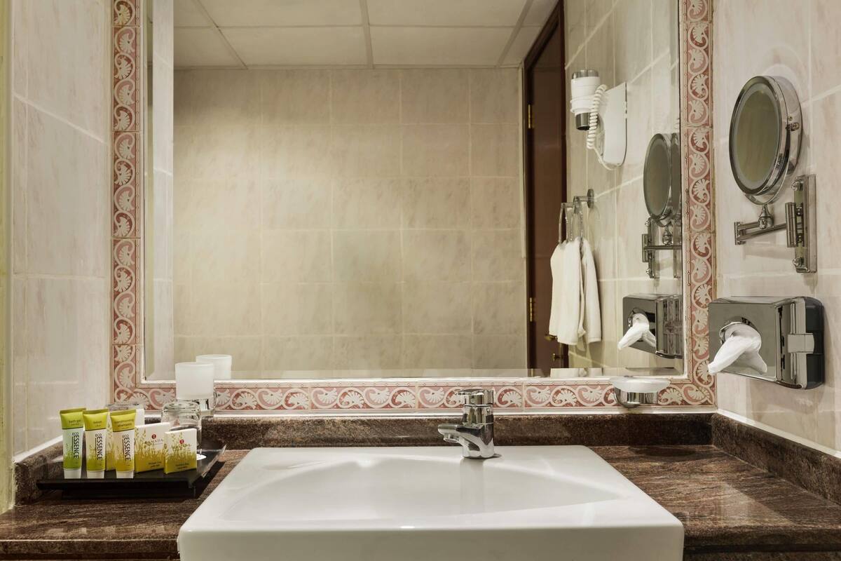Un baño con un espejo grande, un lavabo y artículos de aseo en una bandeja.