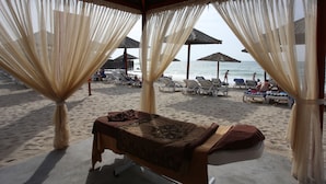 Un espace de massage aménagé sur la plage, comprenant une table de massage, des serviettes et des chaises de plage.