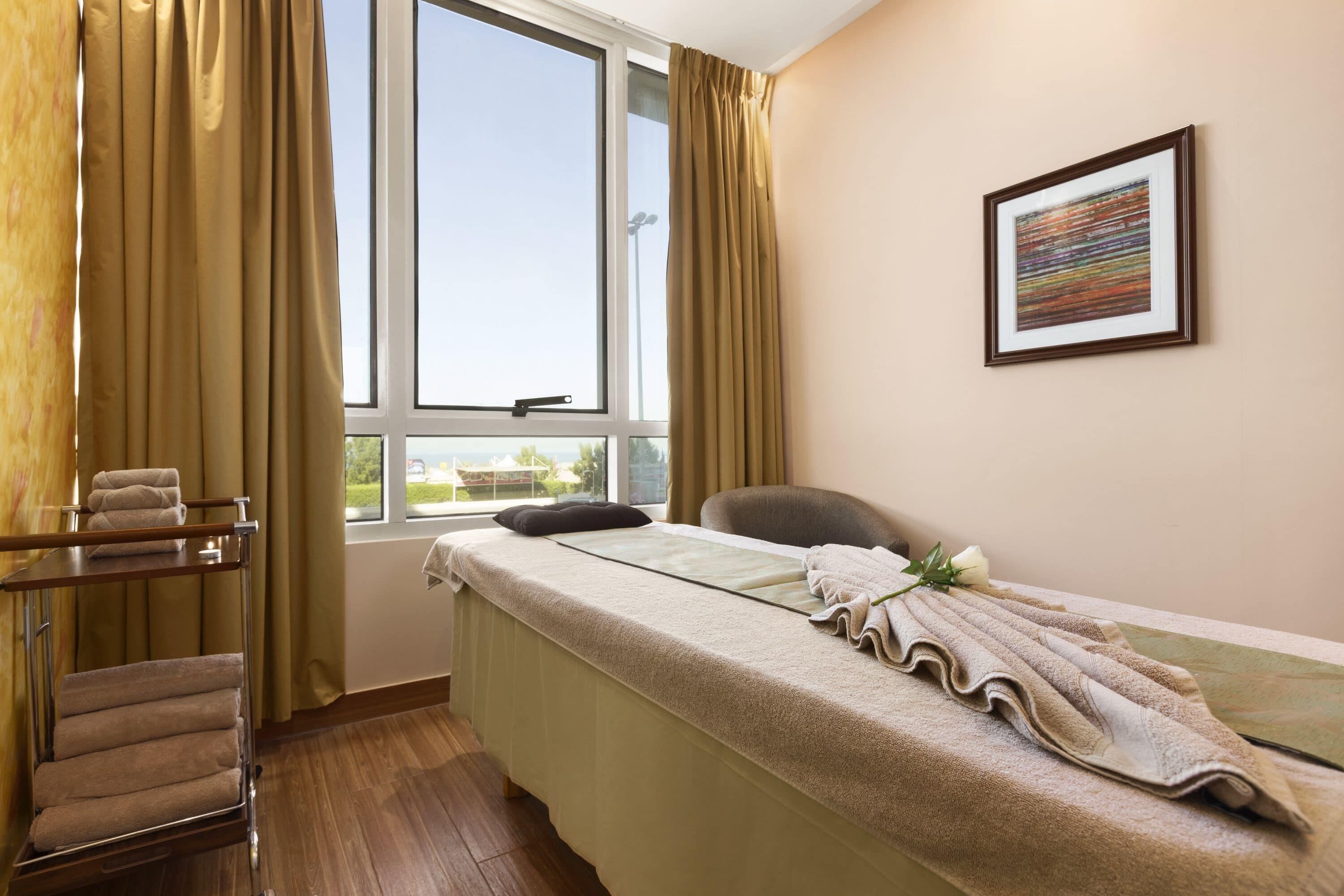 A room with a bed, a chair, a window with curtains, a towel rack, and a framed picture on the wall.