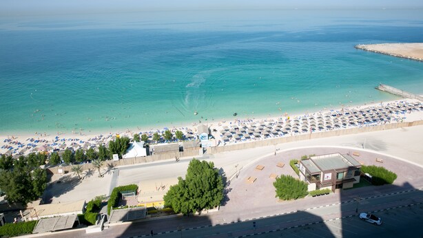 Vue aérienne d’une plage avec un espace de stationnement, des parasols et un petit bâtiment.