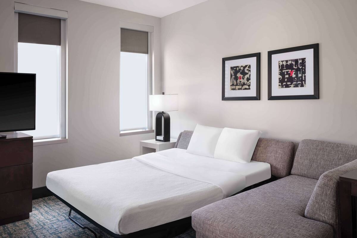 Een hotelkamer met een bed, een bank, een televisie en twee foto's in lijsten aan de muur.