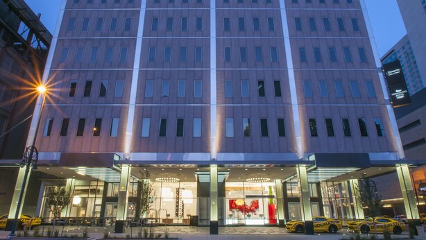 Un hôtel moderne, avec une façade en verre, de nombreux étages et une entrée imposante surmontée d’une enseigne rouge.