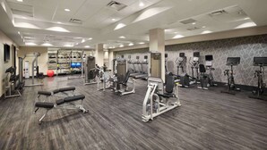 Une salle de sport équipée de divers appareils d’exercice, de bancs et d’un téléviseur fixé au mur.
