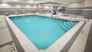 Une grande piscine intérieure avec des lignes de nage clairement délimitées, un espace vestiaire et un espace détente avec des tables et des chaises.