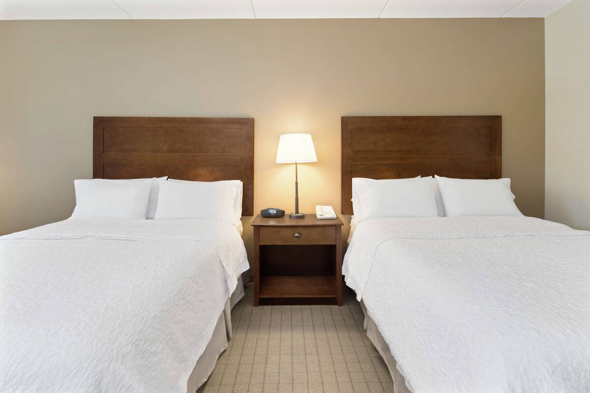 A hotel room with two beds, a nightstand with a lamp, and a telephone.