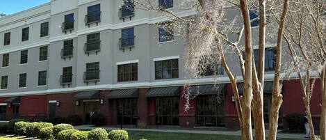 A multi-story hotel with a symmetrical facade, large windows, and a landscaped front yard with trimmed bushes.